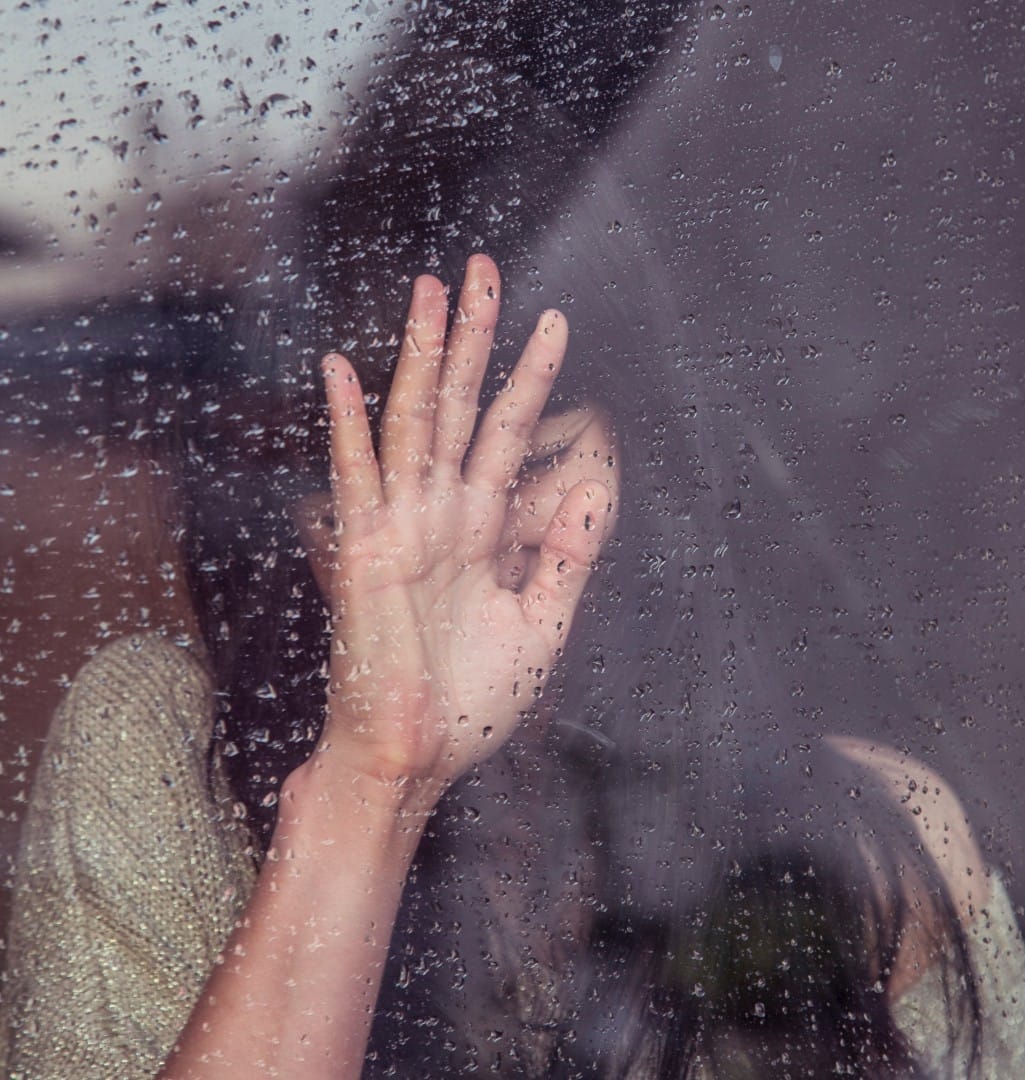 woman with hand on rainy window