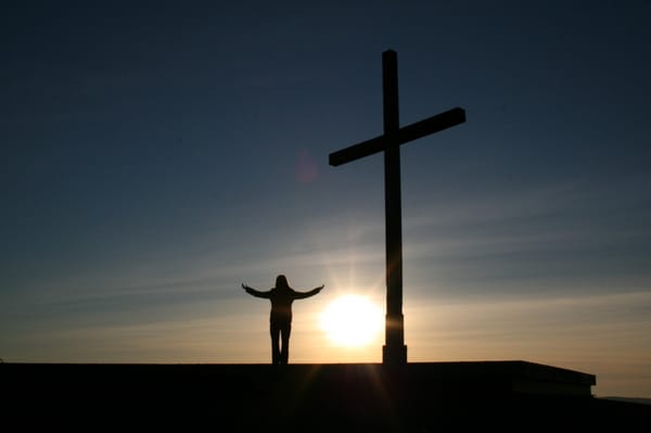 man standing on hill with cross
