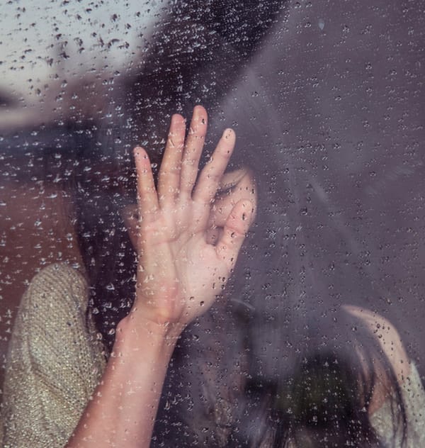 woman with hand on rainy window